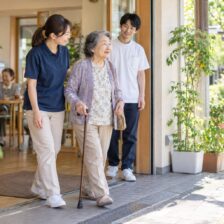 デイサービスから地域へ出かける高齢者を介護スタッフと理学療法士が見守るイメージ
